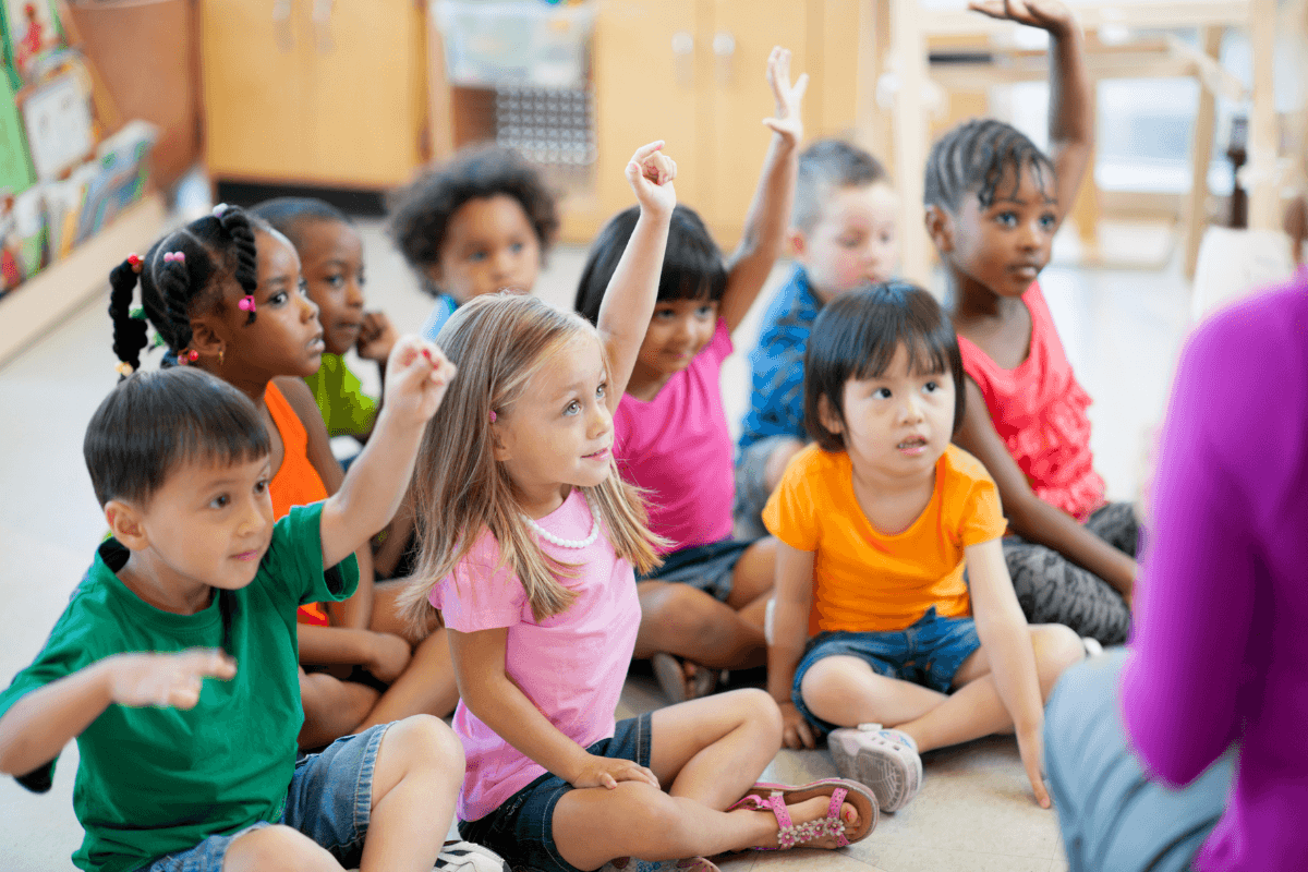 preschool children sitting on floor raising hands