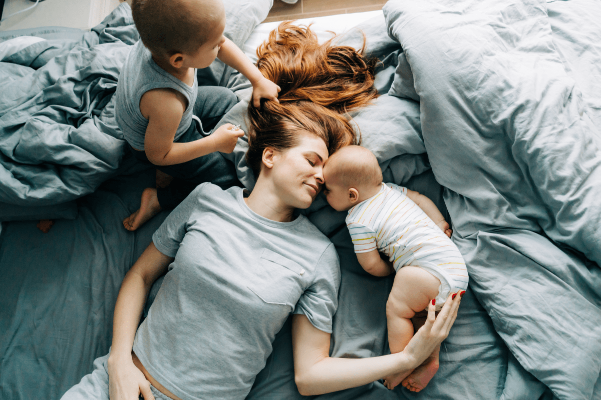 stay-at-home mom on bed with two children surrounding her