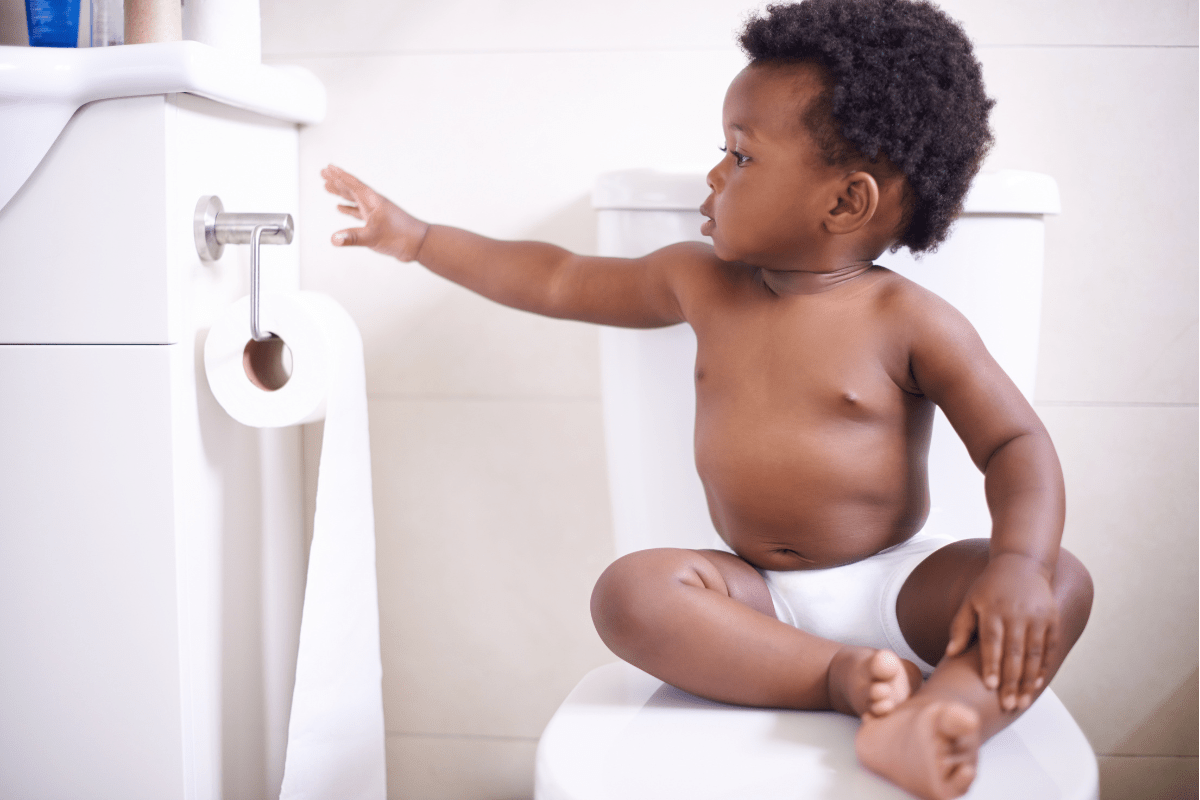child sitting on closed toilet seat reaching for toilet paper (potty training and potty learning)