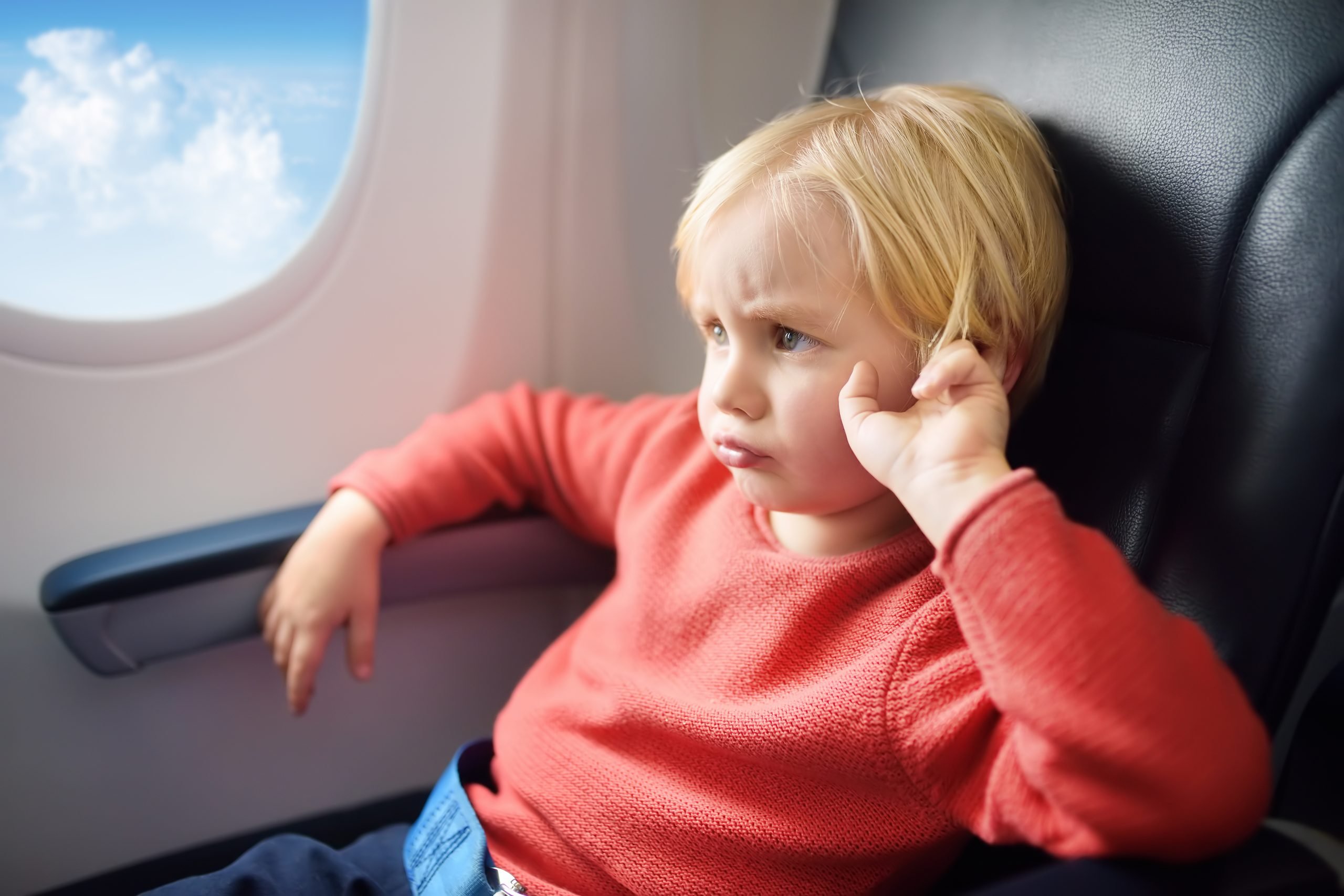 young boy sitting in airplane window seat (airplane travel with kids, tantrum)