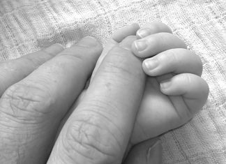 black and white image of an infant's fingers grasping an adult's