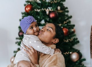 Black woman holding and kissing a baby in front of a Christmas tree