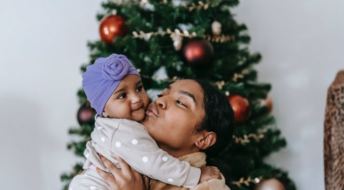 Black woman holding and kissing a baby in front of a Christmas tree