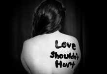 black and white photo of a woman with a bare back with the phrase "Love shouldn't hurt" painted on her skin