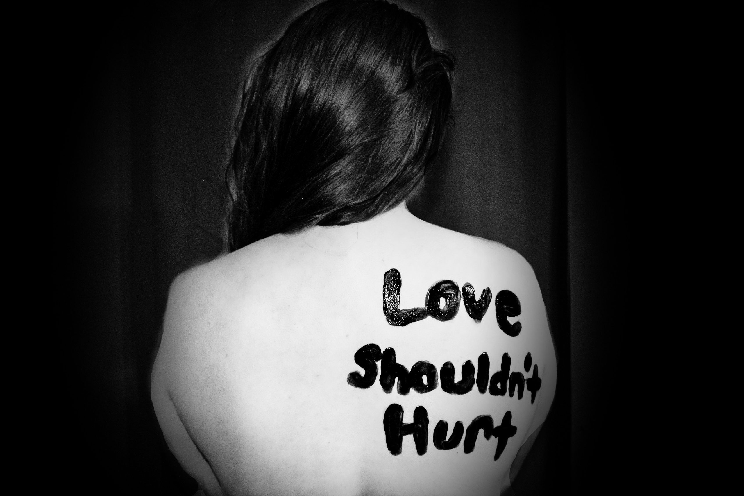 This image is a black and white photo of a woman with a bare back with the phrase "Love shouldn't hurt".