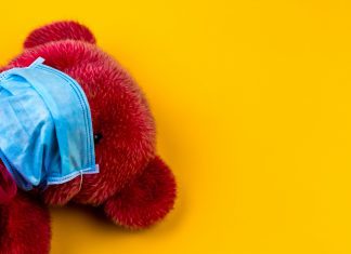 Yellow background with red stuffed animal bear wearing facemark
