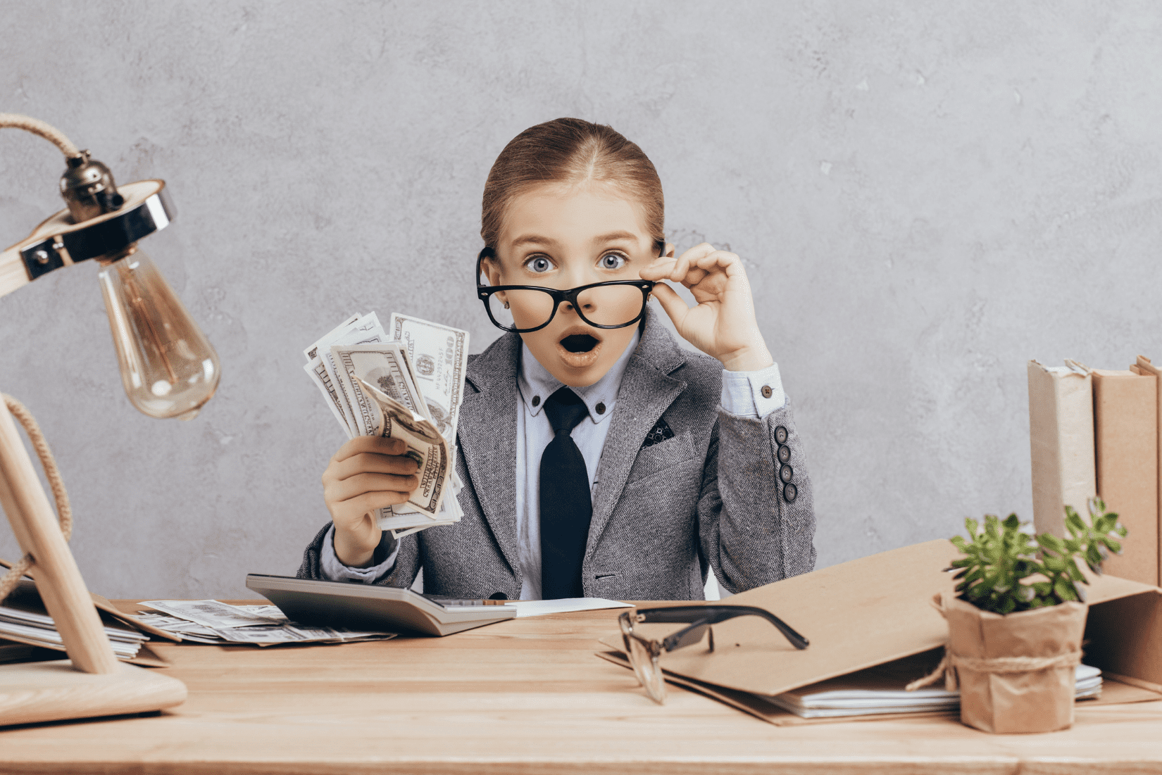 Child, in a business suit with glasses, holding money. She is surprised.