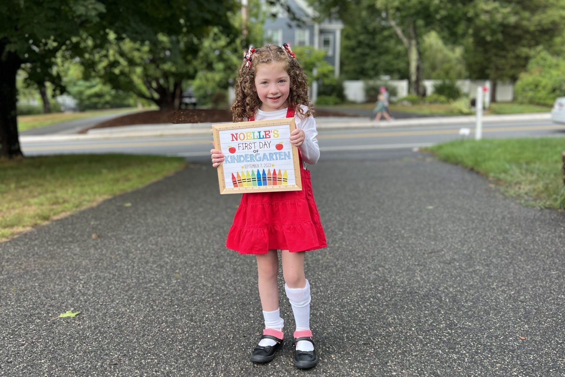 girl in red dress holding a first day of school sign