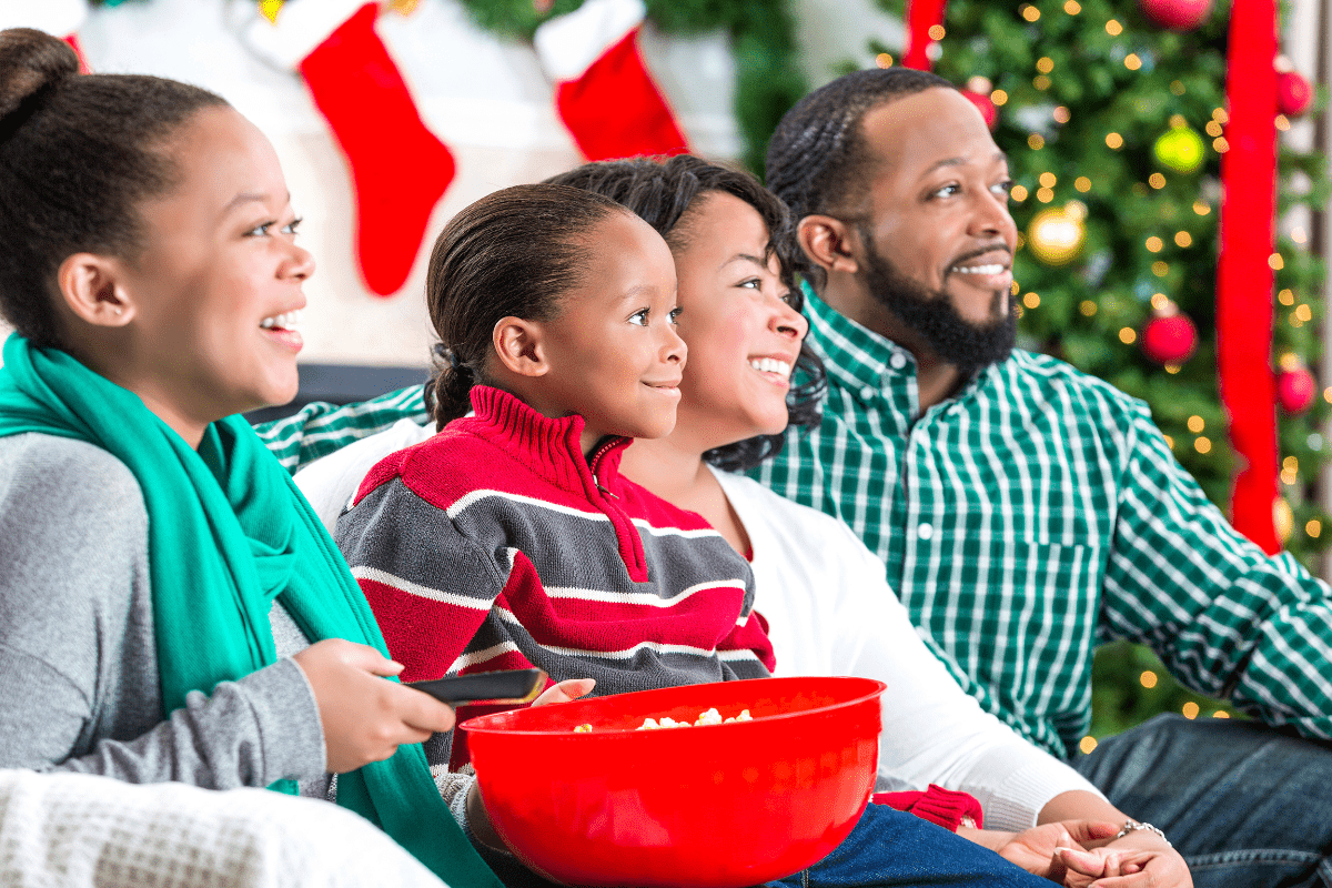 family sitting together with a red bowl of popcorn, watching a holiday Christmas movie