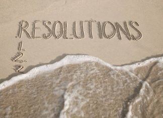 "Resolutions" written in sand with a wave about to wash the letters away, illustrating the idea that the new year doesn't have to bring a "new you"