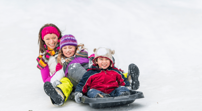 mother and two children sitting together on a gray sled on a snowy hill