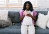 pregnant woman sitting on couch with pen and notebook in hand, thinking about what to choose for her child's last name