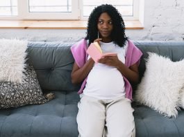 pregnant woman sitting on couch with pen and notebook in hand, thinking about what to choose for her child's last name