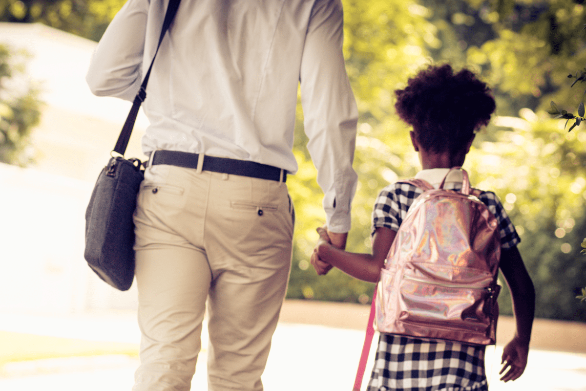 child wearing pink backpack holding hands with her father on the way to the first day of school