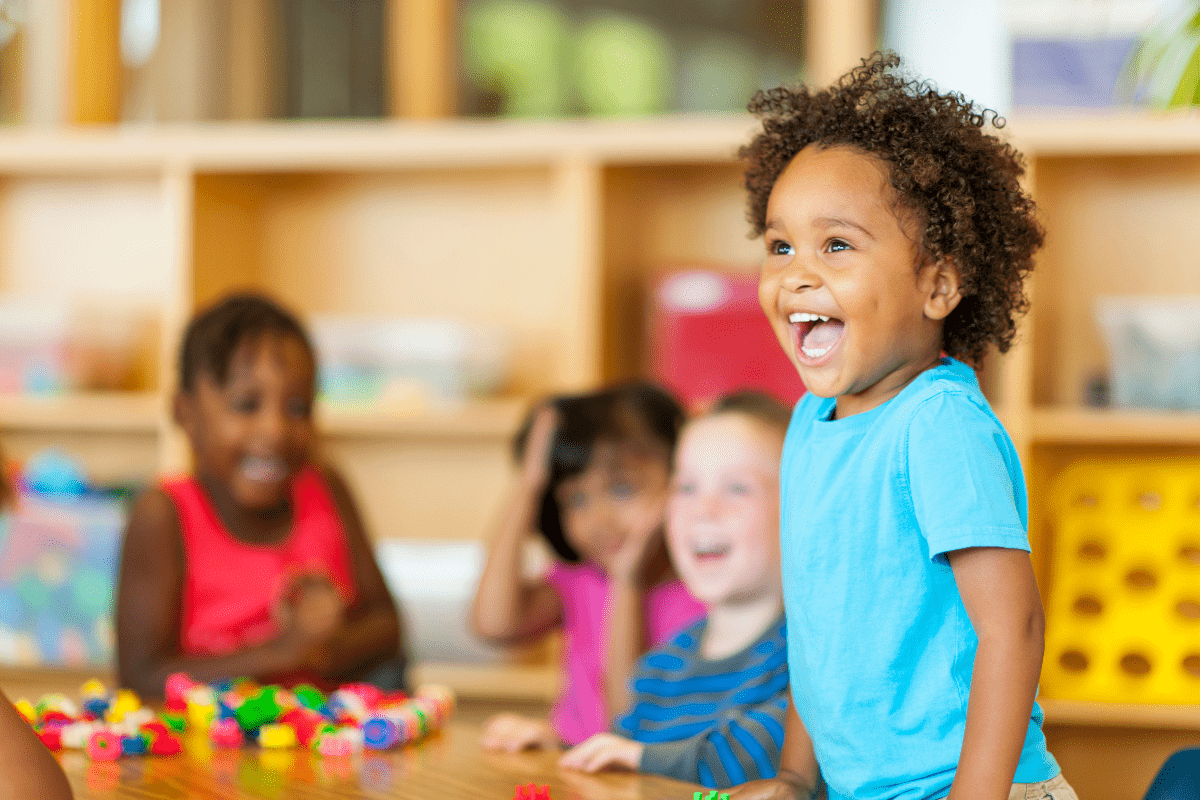 smiling child at preschool surrounded by a table full of friends