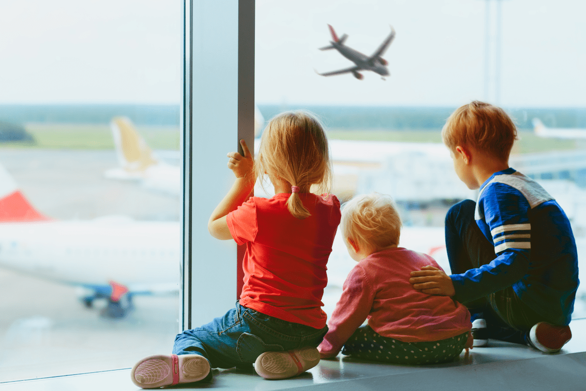 three children watching airplanes from inside an airport