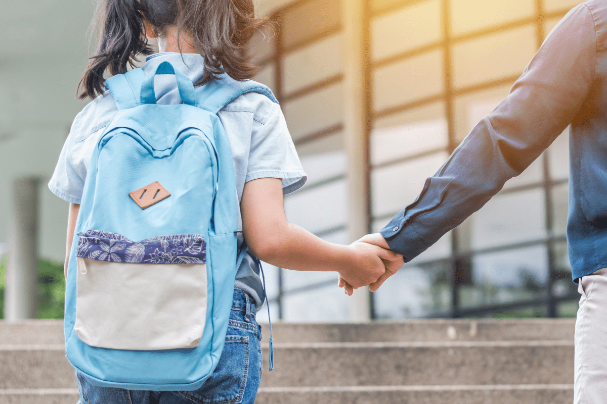 child and parent holding hands, walking to school