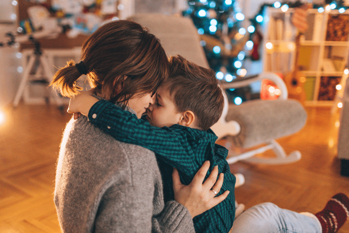 mom and child hugging near Christmas tree (single parent holiday traditions)