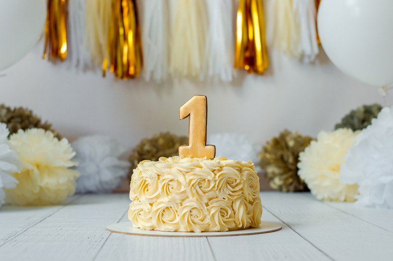 birthday cake with number one candle in front of metallic streamers
