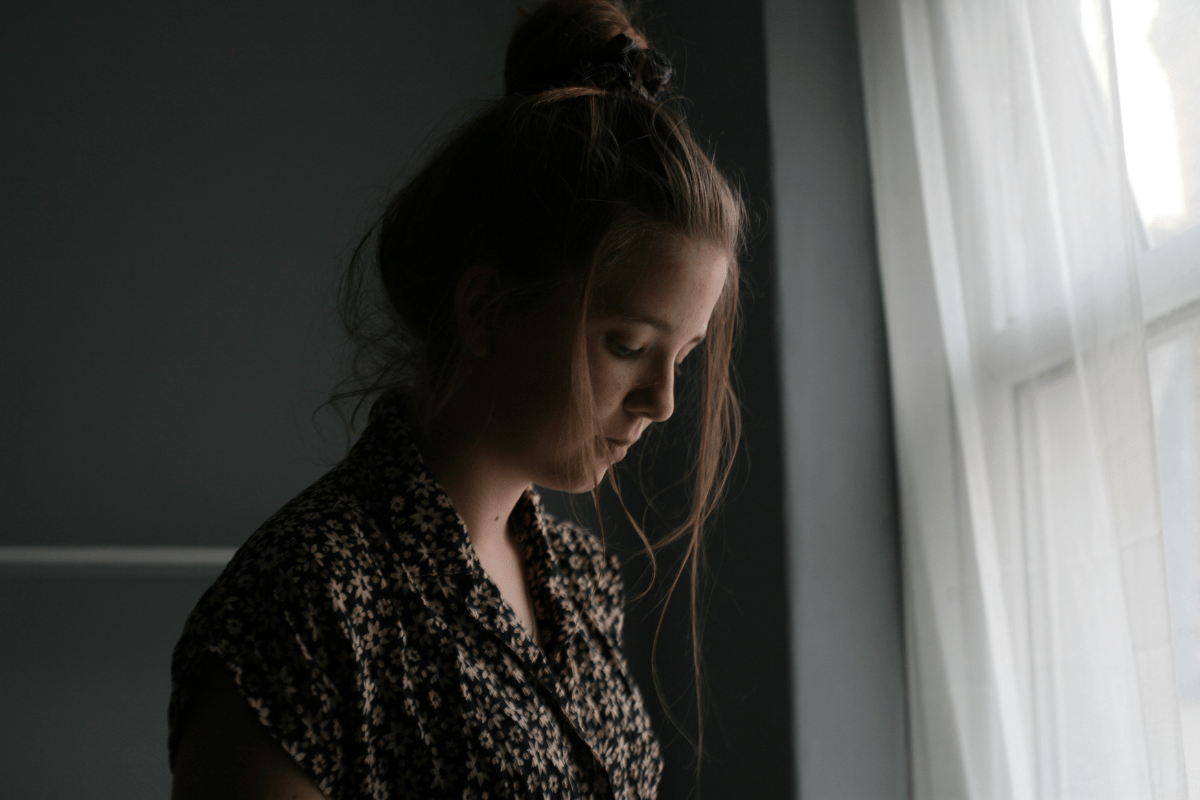 woman looking sad beside window (mothering with chronic illness, multiple sclerosis)