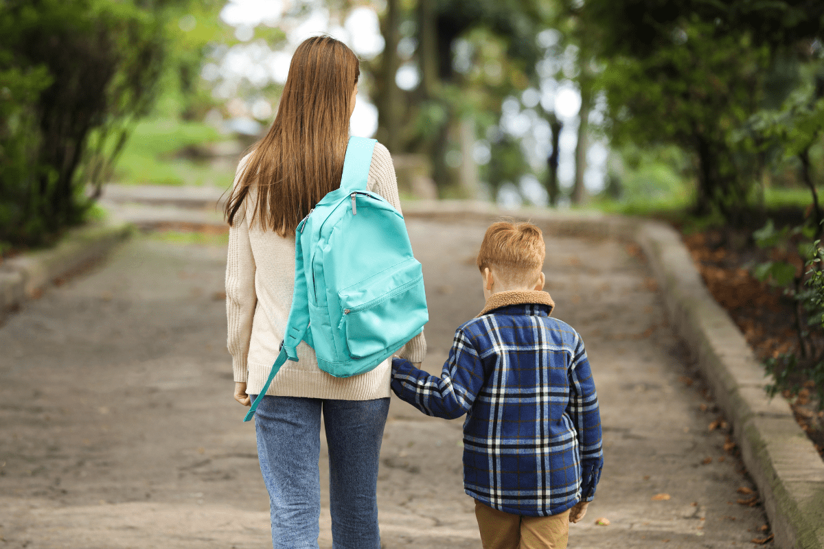 mom with backpack holding hands with school-aged child (kindergarten and working mom)