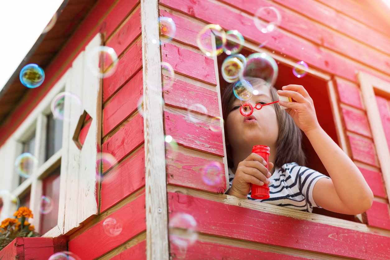 child inside a backyard playhouse (backyard structure ideas for kids)