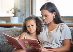 Loving hispanic mother and her little daughter sitting at home and reading a storybook together. raising bilingual children